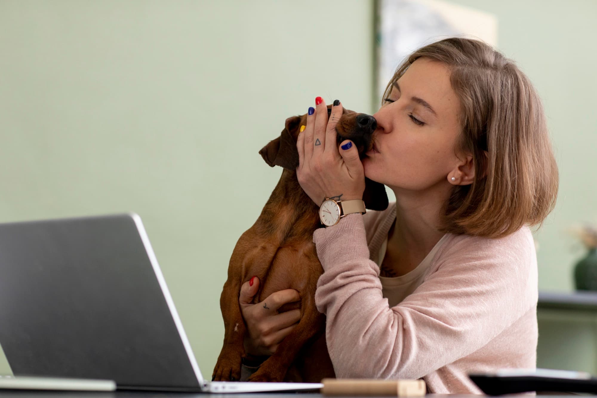 Una mujer besa a su perro salchicha mientras trabaja en su laptop